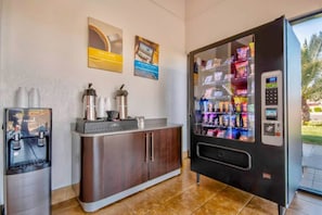 A vending machine stocked with snacks, a coffee machine, and a water dispenser in a commercial setting.