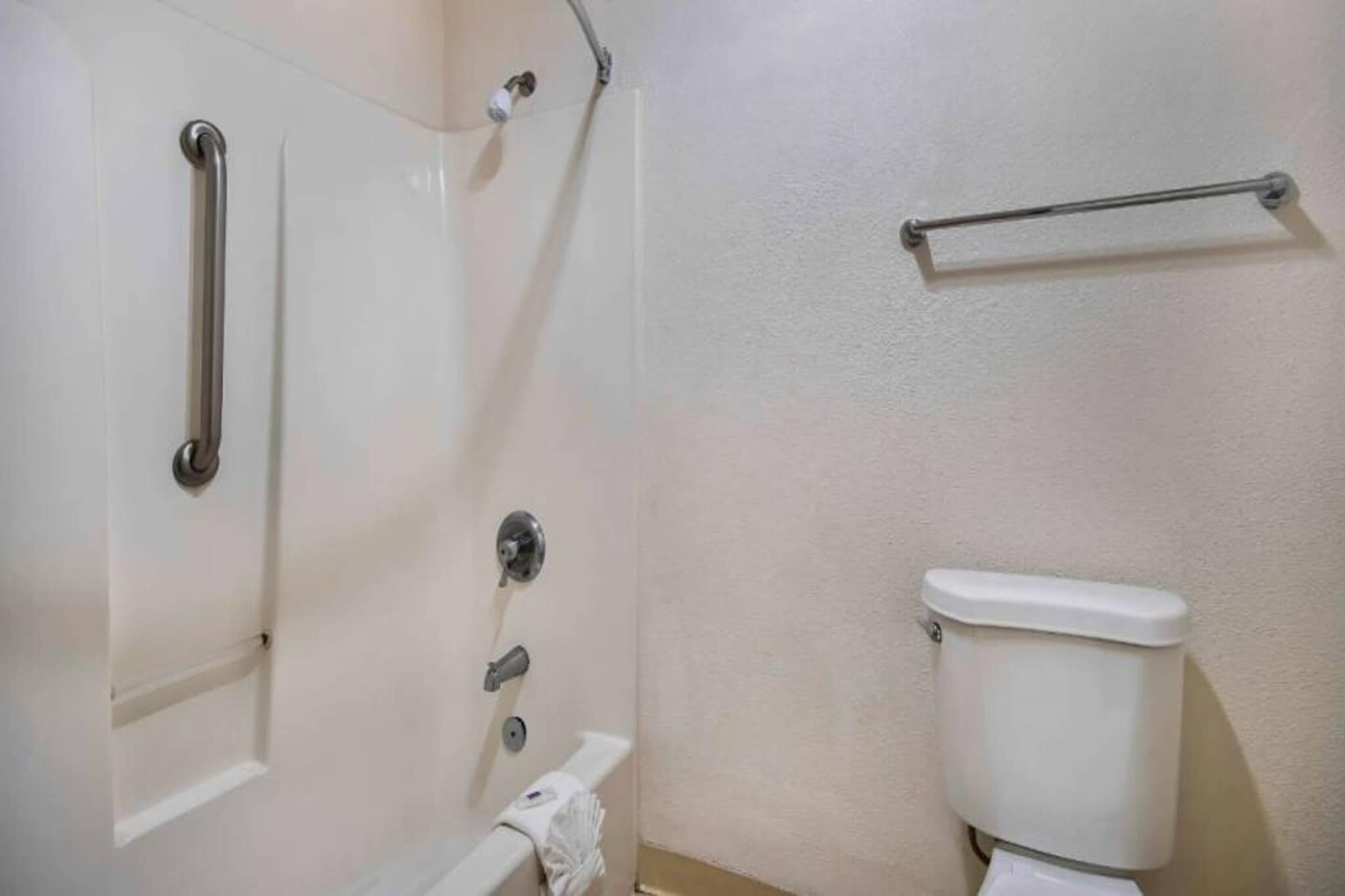 Un baño con inodoro blanco, zona de ducha con barra de apoyo y un perchero.