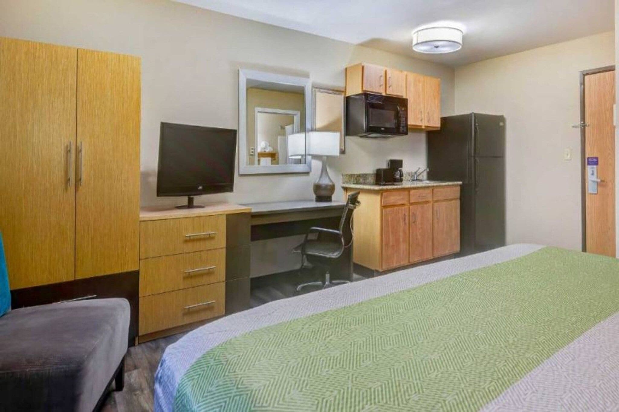 A hotel room with a bed, a desk with a computer, a television, a microwave, and a refrigerator.