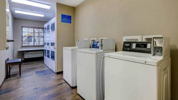 A laundry facility with multiple washing machines and dryers, a bench, and a window with blinds.