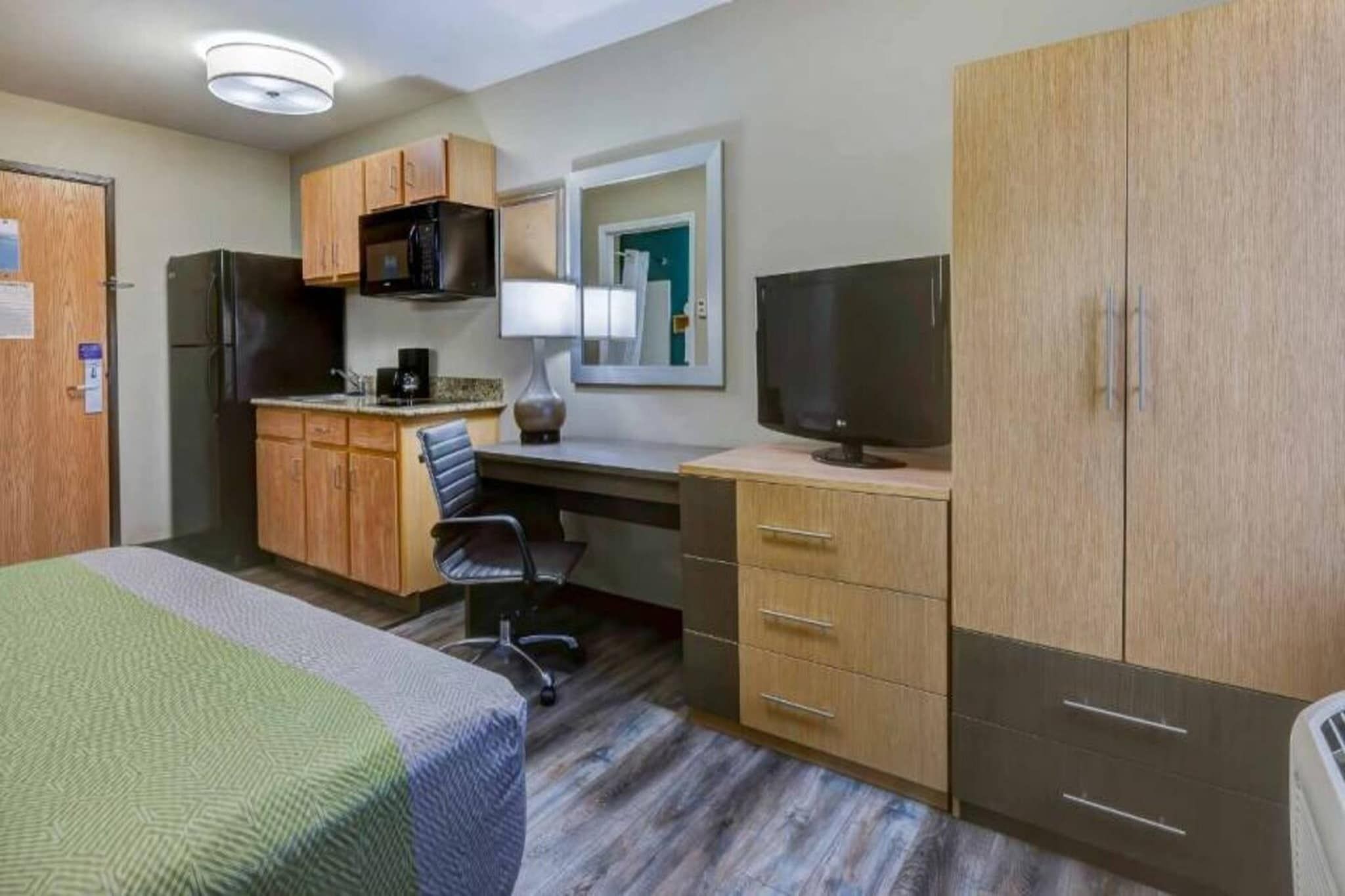 A hotel room with a bed, a desk with a chair, a television, a microwave, and a refrigerator.