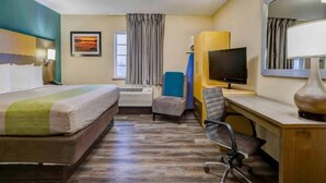 Une chambre d’hôtel équipée d’un lit, d’un bureau, d’une chaise, d’une télévision et d’une fenêtre avec des rideaux.