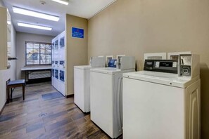 A laundry room with multiple washing machines and dryers, a bench, and a window with blinds. - 1 King Bed | Non-Smoking, Kitchen (Lenexa)