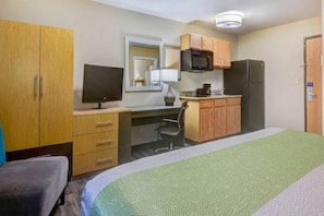 Une chambre d’hôtel équipée d’un lit, d’un bureau avec un ordinateur, d’une chaise, d’une télévision, d’un four à micro-ondes et d’un réfrigérateur.