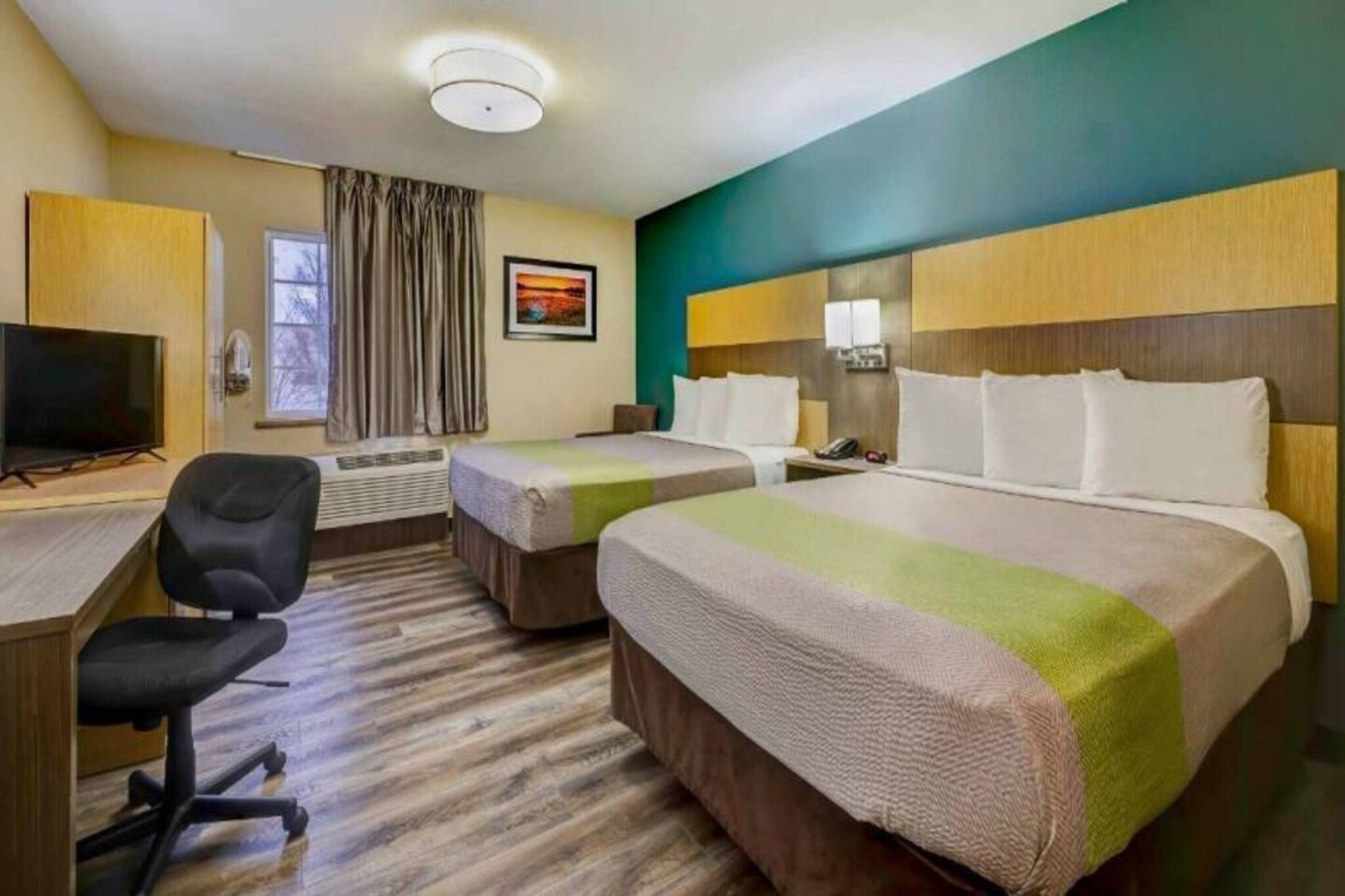 A hotel room with two beds, a desk with a chair, a television, and a window with curtains.