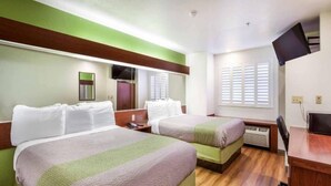 Habitación de hotel con dos camas, televisión, escritorio y ventana con persianas.