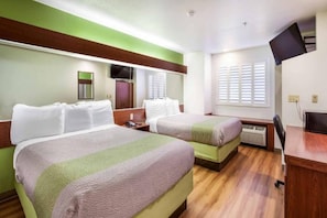 Een hotelkamer met twee bedden, een televisie, een bureau en een raam met zonwering.