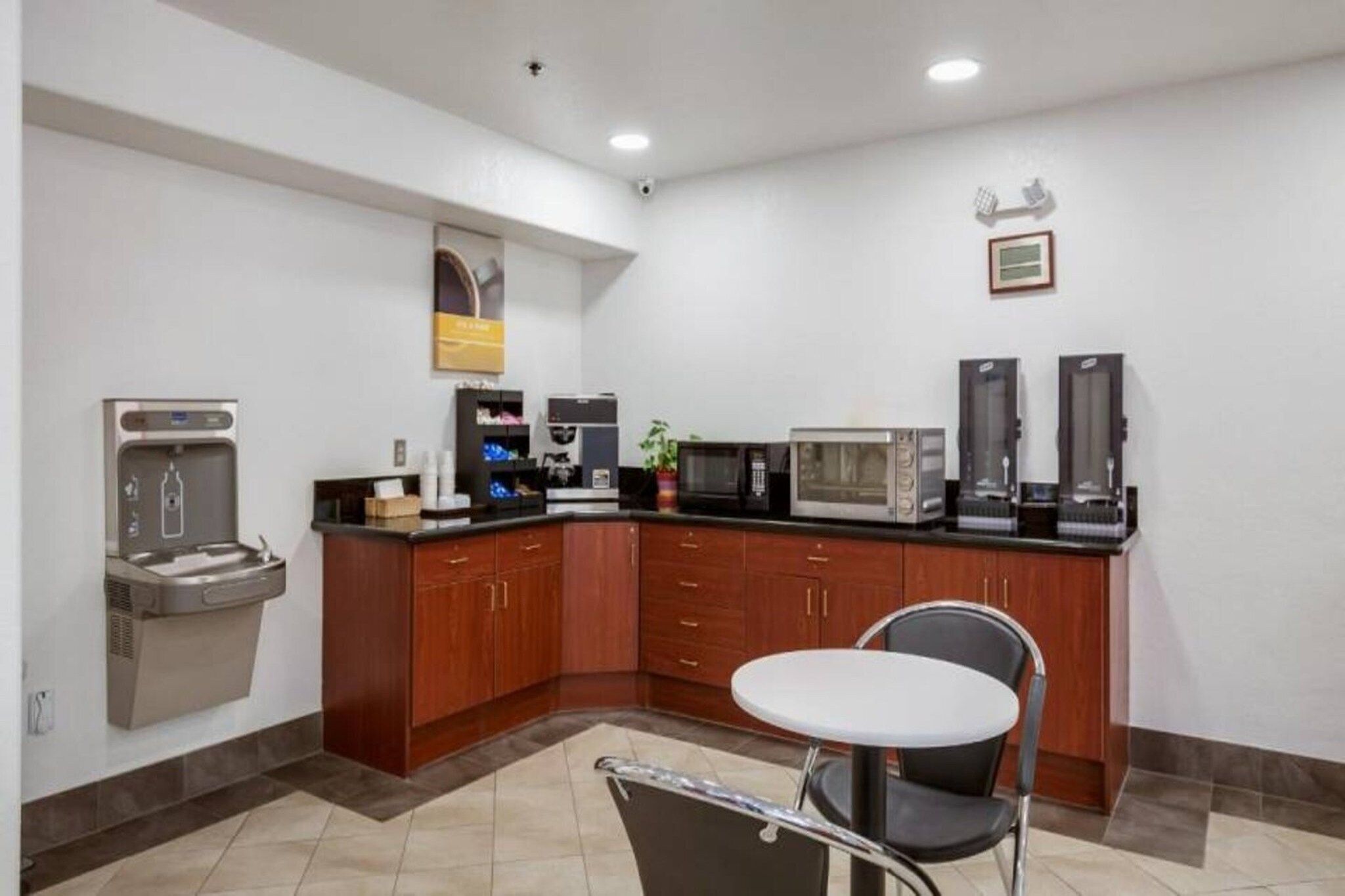 A small kitchenette with a coffee machine, microwave, toaster, and a single chair.