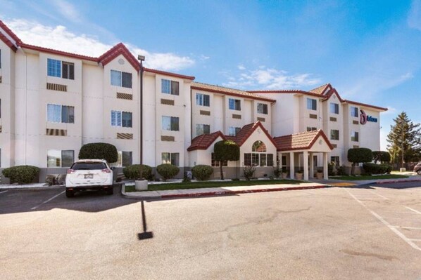 A multi-story hotel with a red-tiled roof, a parking lot, and a white car parked in front.