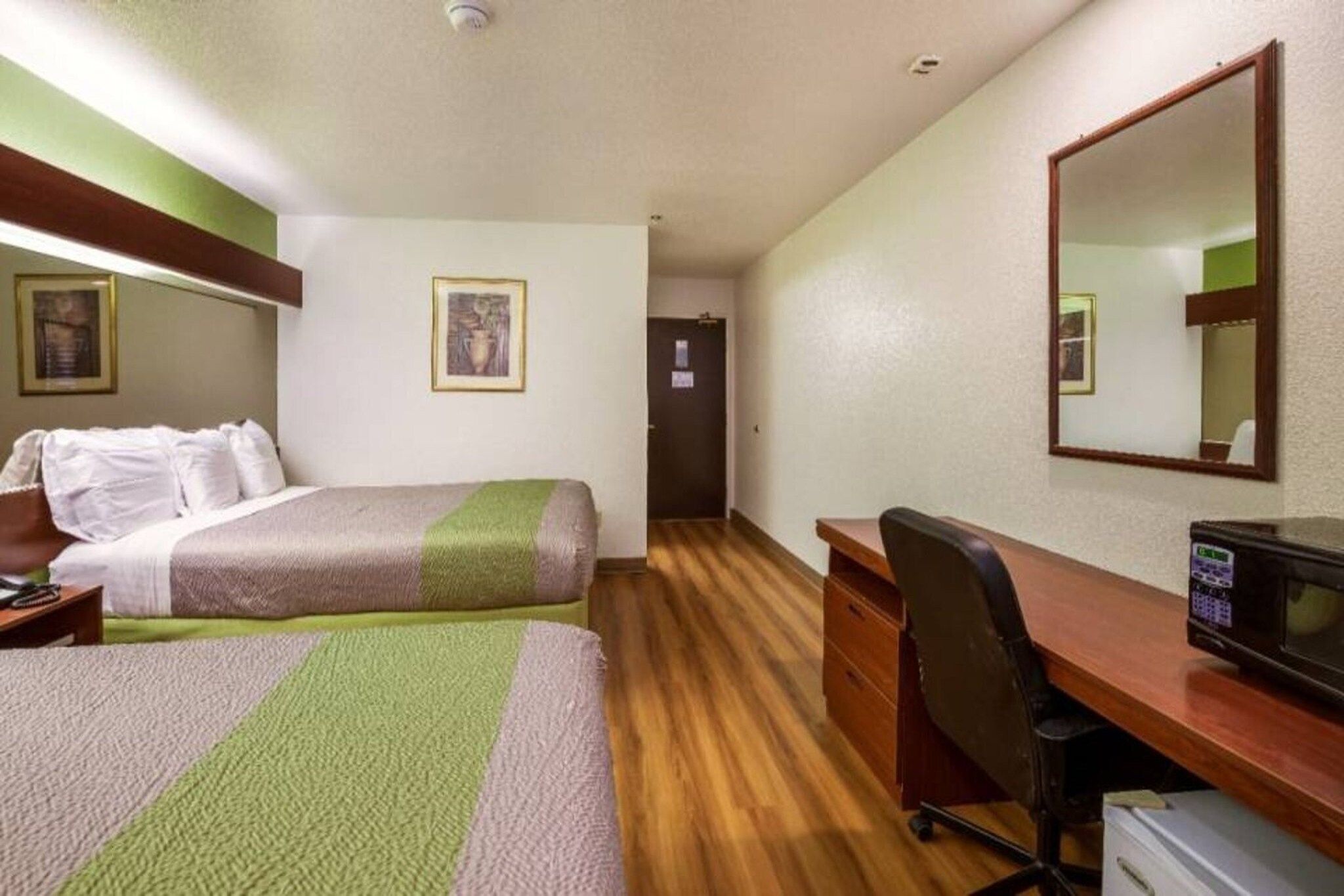 Ein Hotelzimmer mit zwei Betten, einem Schreibtisch, einem Stuhl, einer Mikrowelle und einer Tür zu einem weiteren Raum.
