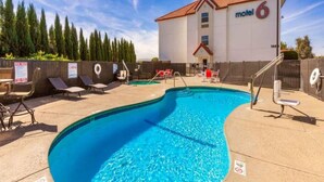 Una piscina con sillas de descanso y un motel al fondo.