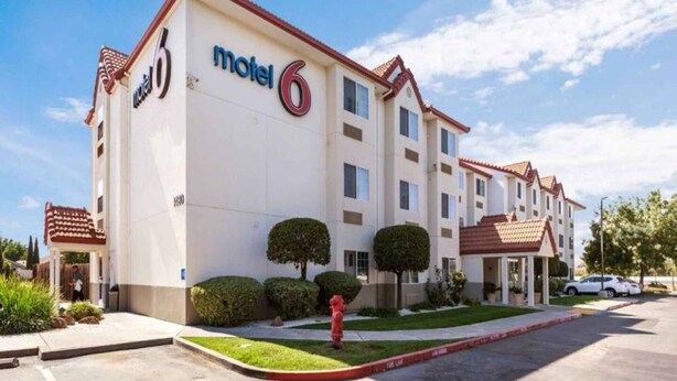 Un motel con un llamativo letrero de 'Motel 6', múltiples ventanas y un estacionamiento.