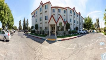 A multi-story hotel with a central entrance, parking lot, and surrounding greenery.