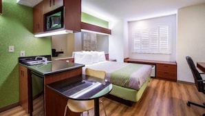 Habitación pequeña con cama, escritorio y silla. Hay un televisor montado sobre el escritorio y una ventana con contraventanas.