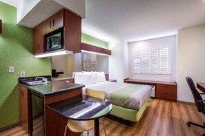 A compact room with a bed, a desk, and a chair. There is a television mounted above the desk and a window with shutters. - Queen Bed|Suite,Nsmk,Micfridge,Sofa-Bed (Dixon)