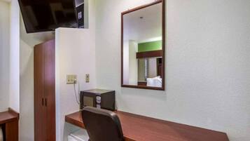 Ein Hotelzimmer mit einem Holztisch, einem Sessel, einem an der Wand befestigten Fernseher, einer Mikrowelle und einem kleinen Kühlschrank.