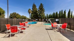 Zona de piscina exterior con sillas y mesas rojas, rodeada por una valla y árboles.