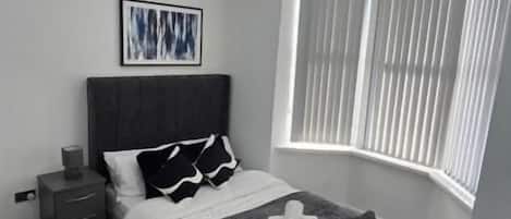 A bedroom with a bed, bedside tables, a window with blinds, and a ceiling light fixture.