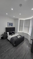 Un dormitorio con cama, mesitas de noche, una ventana con persianas y una lámpara de techo.