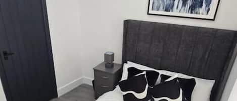 A bedroom with a bed, a bedside table, a nightstand, a door, and a wall-mounted artwork.