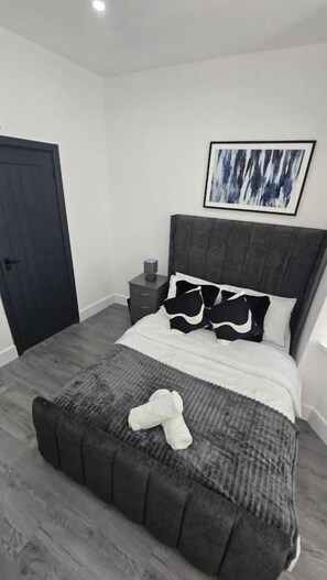 Un dormitorio con cama, una mesita de noche, una puerta y una obra de arte colgada en la pared.