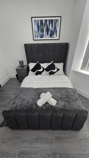 Una cama con cabecera gris, ropa de cama blanca y dos almohadas blanco y negro.