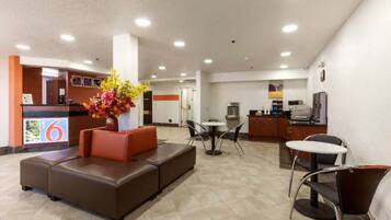 A hotel lobby with a reception desk, seating area, and a kitchenette.
