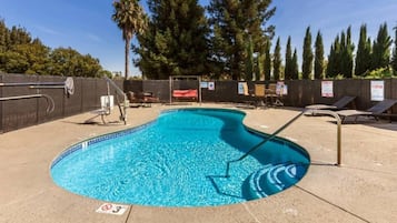 A swimming pool with a diving board, surrounded by lounge chairs and a fence.