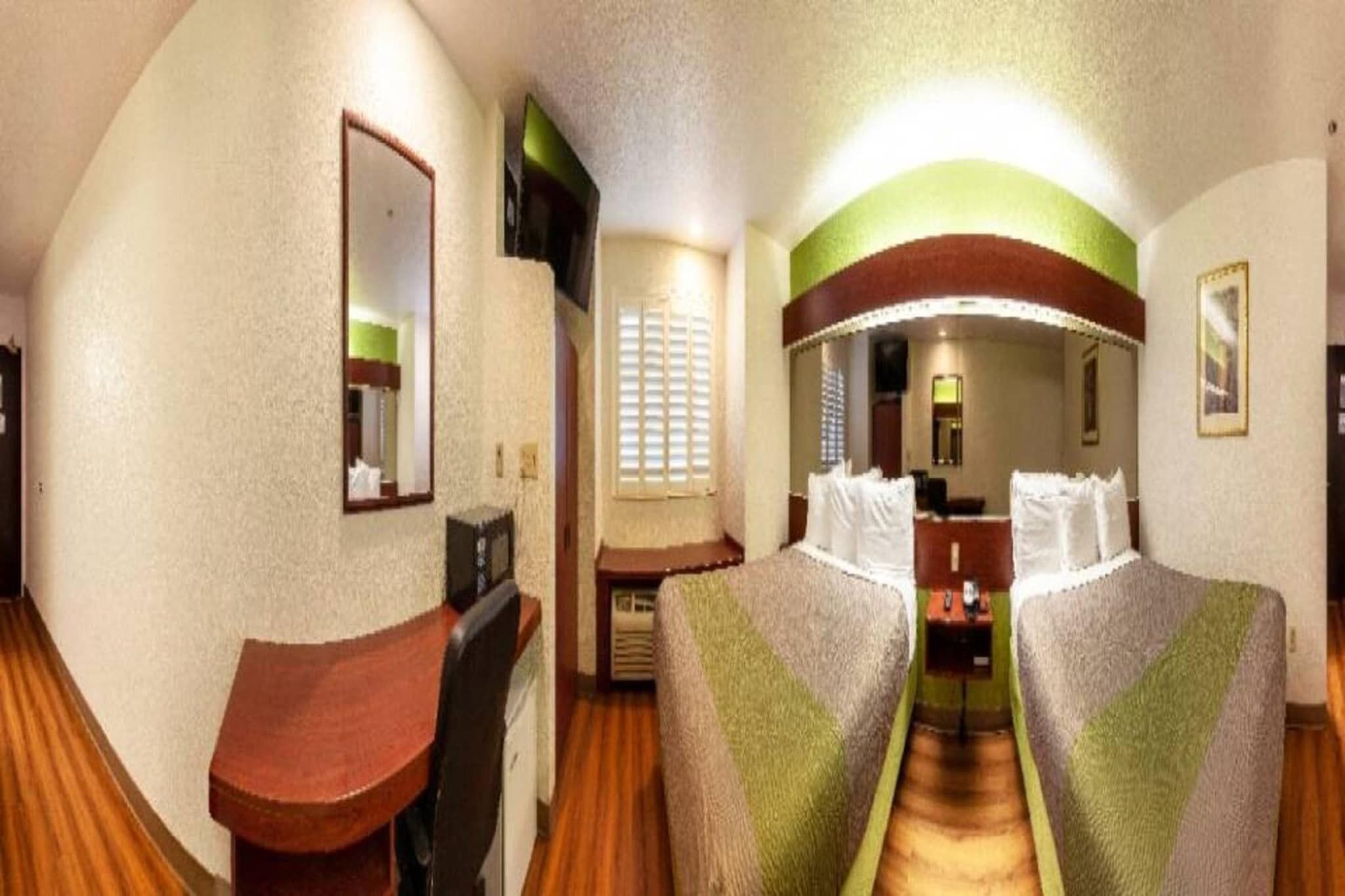 A hotel room with a bed, a desk, a mirror, and a window with blinds.