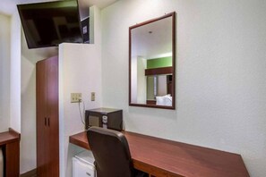 Ein Hotelzimmer mit einem Holztisch, einem Sessel, einem an der Wand befestigten Fernseher, einer Mikrowelle und einem kleinen Kühlschrank.
