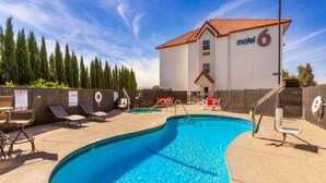 Un área de piscina con sillas de descanso y un motel al fondo.