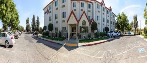Un hotel de varios pisos con entrada principal, estacionamiento y zonas verdes circundantes.