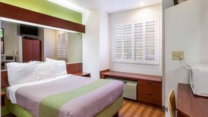 Una habitación de hotel con una cama, un escritorio, una silla, un televisor y una ventana con contraventanas.