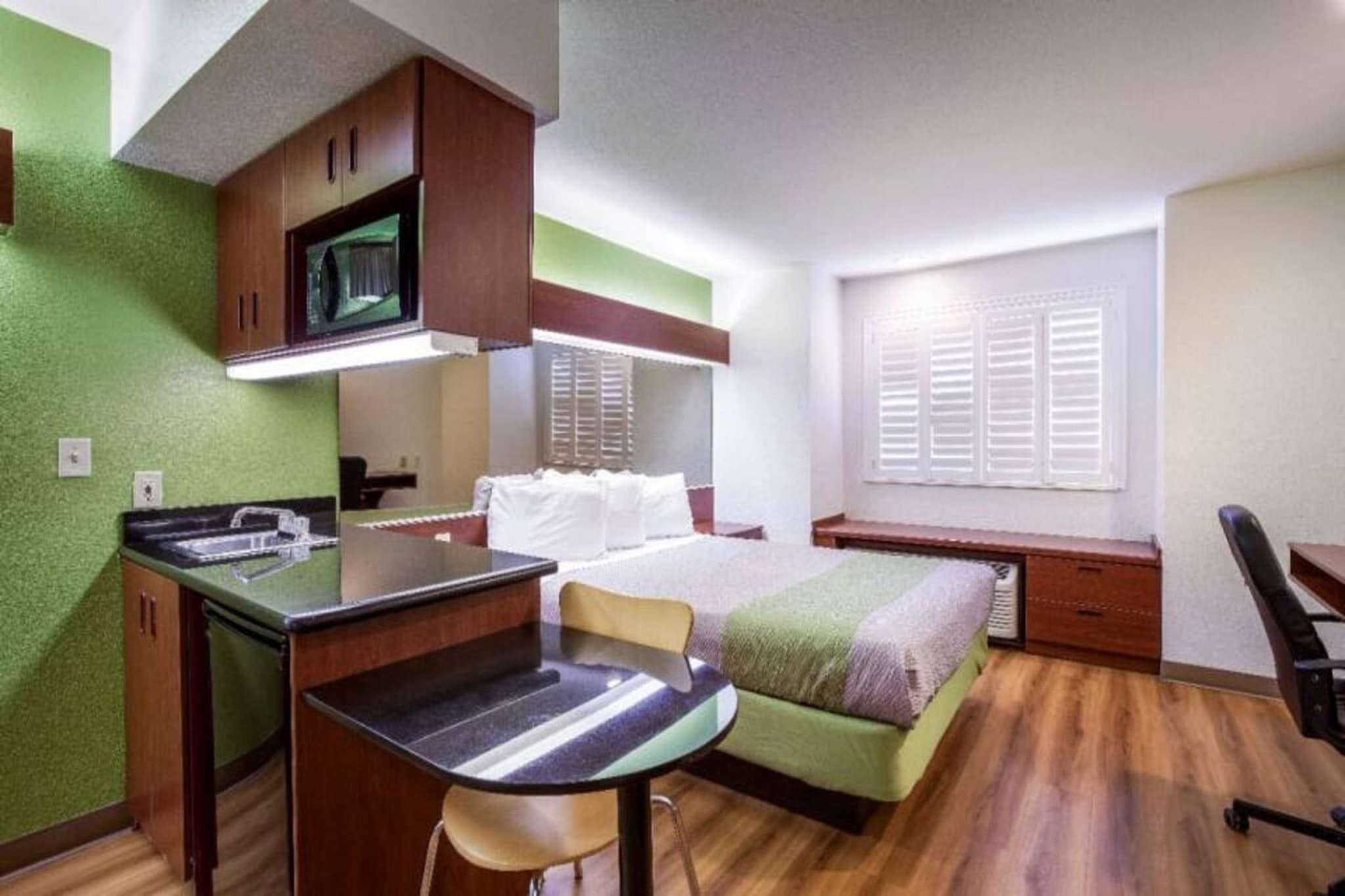 Une pièce compacte comprenant un coin cuisine, un lit, un bureau et une fenêtre avec des volets.