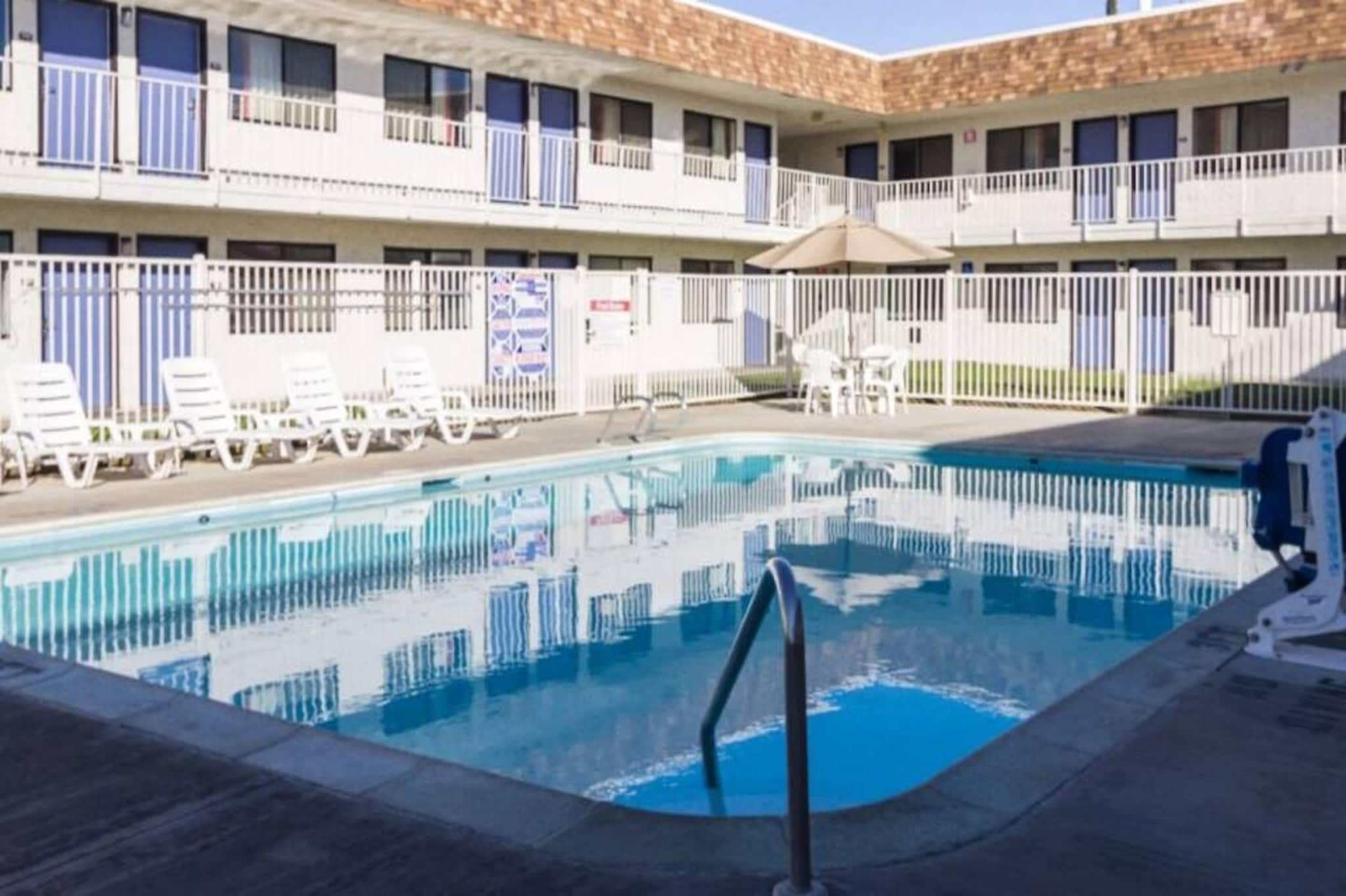 Una piscina con sillas de descanso y un edificio con varios balcones al fondo.