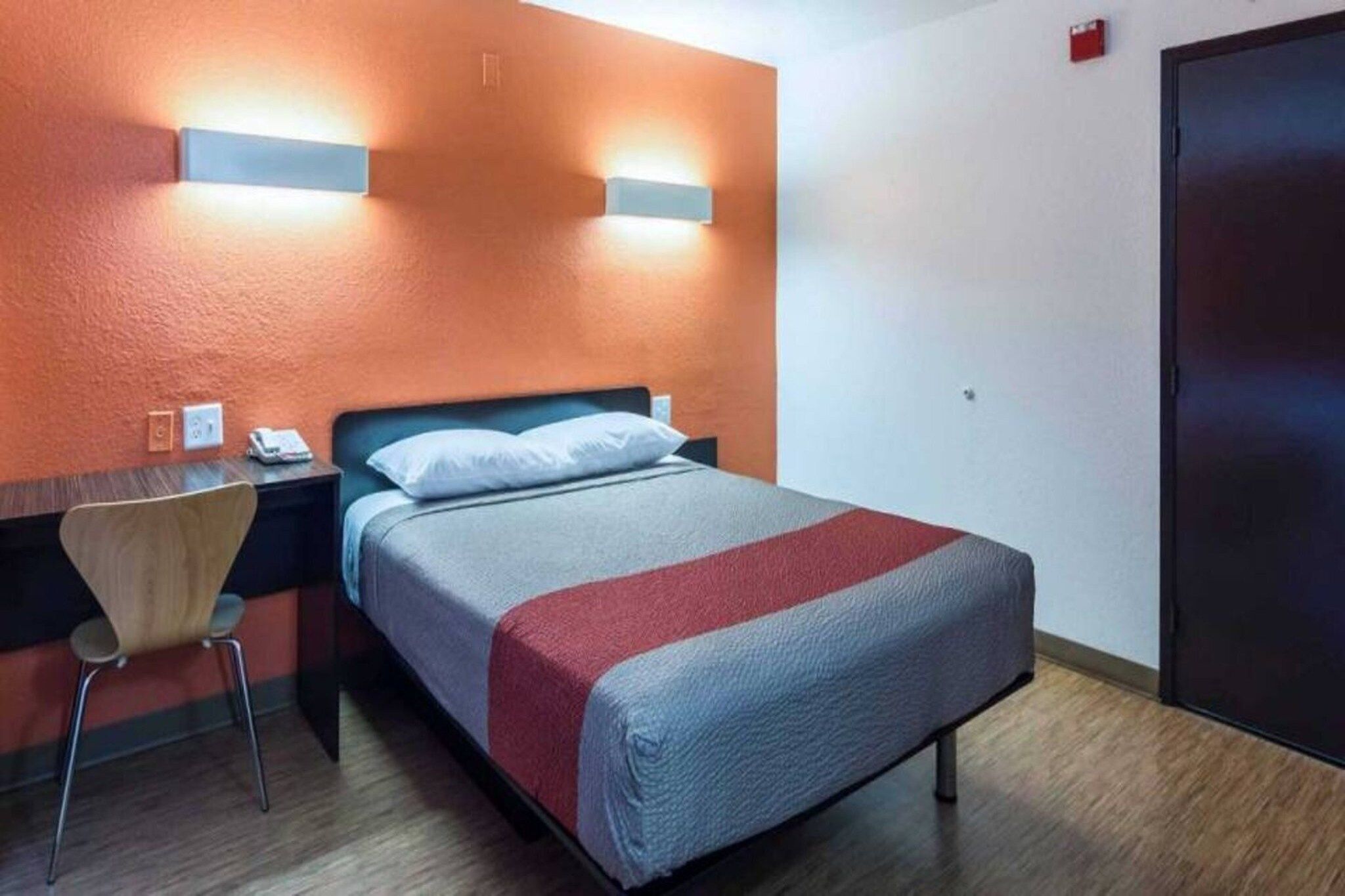 Una habitación de hotel con una cama, una silla, un escritorio y una puerta.