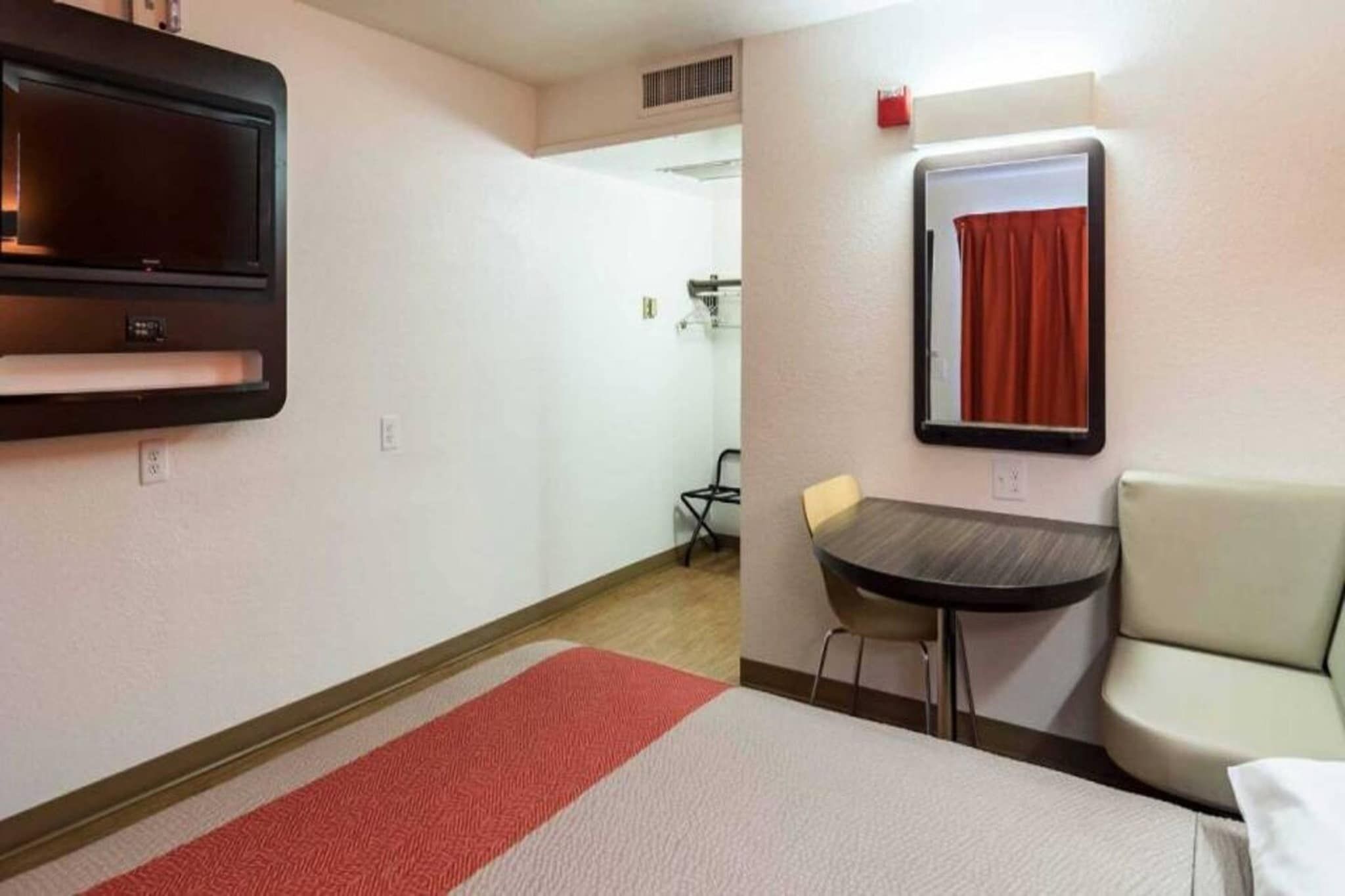 Une chambre d’hôtel avec un lit, une petite table, une chaise, un téléviseur fixé au mur et une fenêtre avec un rideau.