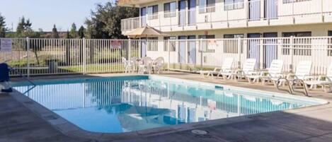 Una piscina con sillas de descanso y un edificio con varias ventanas al fondo.
