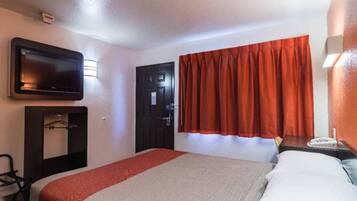A hotel room with a bed, a television mounted on the wall, a door, and a window with curtains.