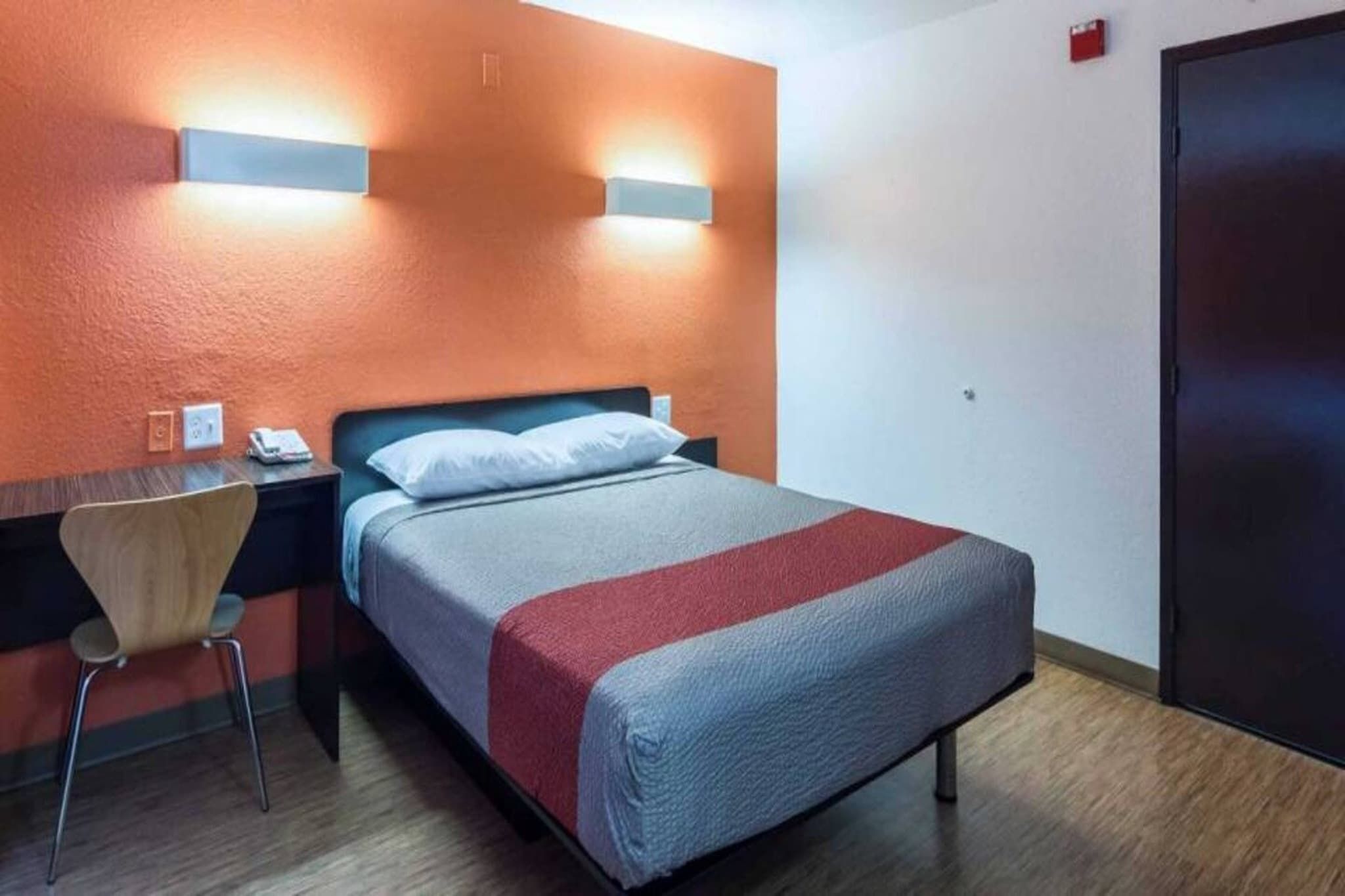 Hotellihuone, jossa on sänky, työpöytä, tuoli ja ovi.