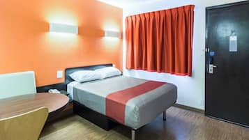 A hotel room with a bed, a desk, a chair, a window with curtains, and a door.