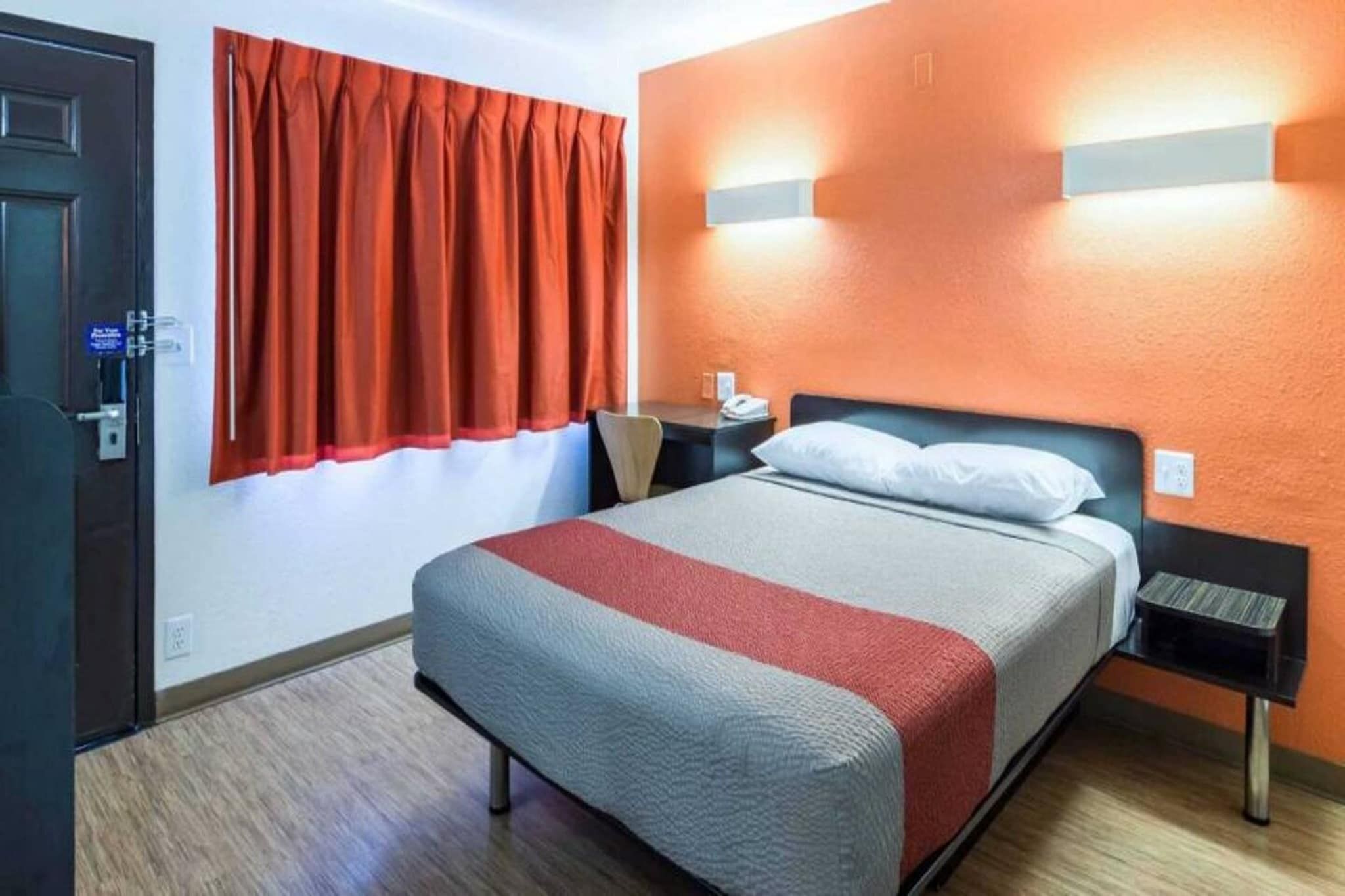 Habitación de hotel con cama, escritorio, silla y ventana con cortinas.