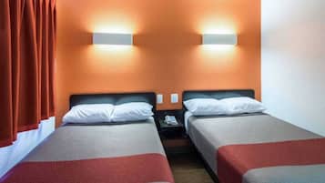 Una habitación de hotel con dos camas individuales, una mesita de noche con un teléfono y una lámpara de pared.