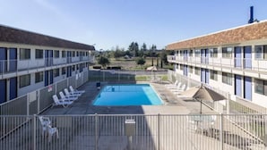 A hotel with a swimming pool, multiple balconies, and a fenced outdoor area with lounge chairs. - 2 Full Beds | Smoking (Oroville)