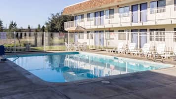 Ein Schwimmbecken mit Liegestühlen und ein Gebäude mit vielen Fenstern im Hintergrund.