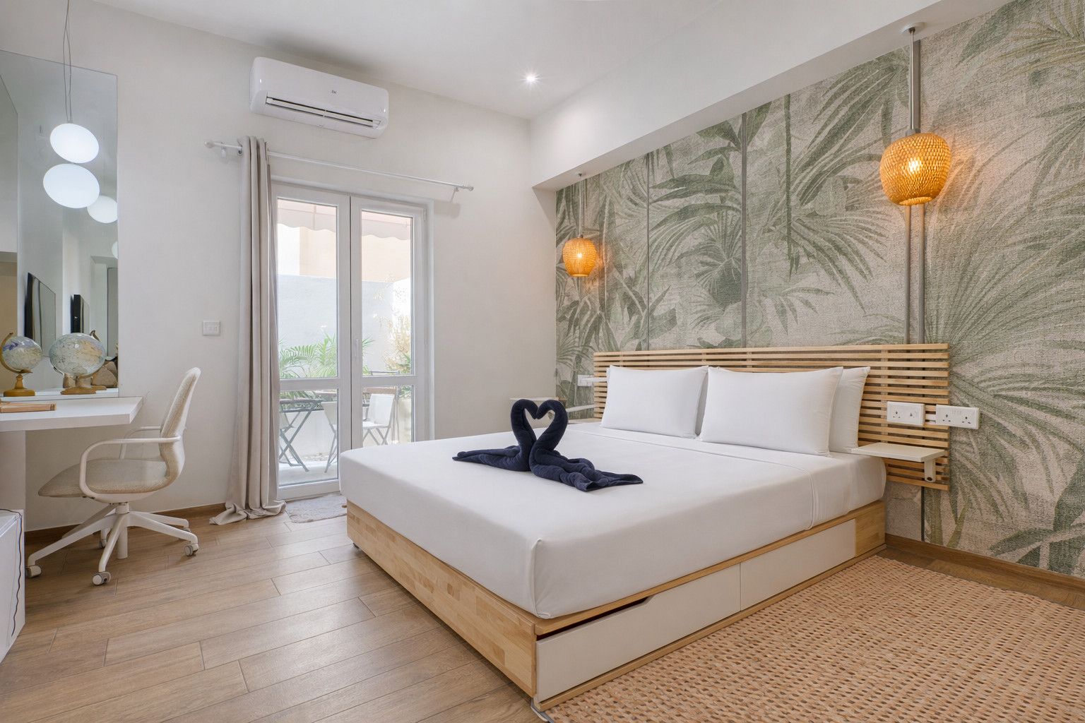 A hotel room with a bed, a desk with a chair, a mirror, and a window.