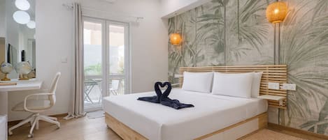 A hotel room with a bed, a desk with a chair, a mirror, and a window.