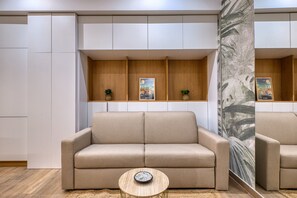 Una sala de estar moderna con un sofá color crema, una pequeña mesa redonda de madera y dos estantes empotrados con objetos decorativos.