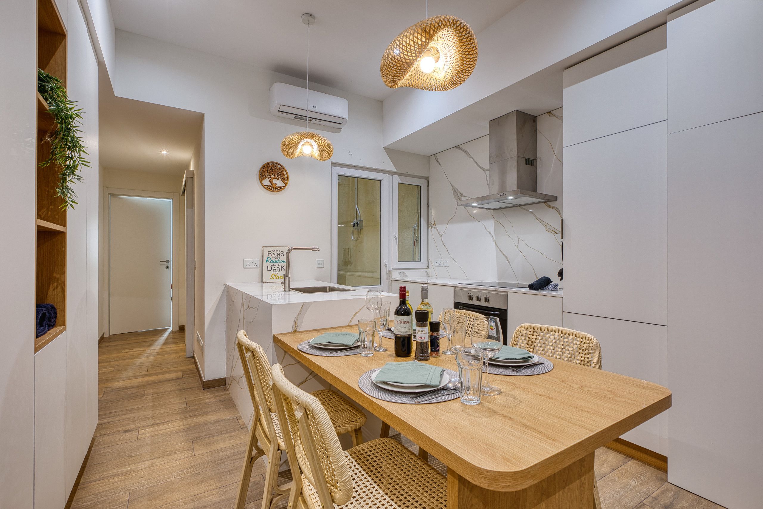 A modern kitchen with a wooden dining table, wicker chairs, and a built-in oven.