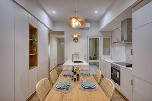 Una cocina moderna con comedor, con una mesa de madera dispuesta para cuatro, una lámpara colgante y un horno empotrado.